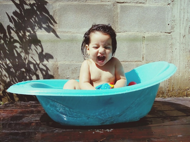 Fröhliches, hemdloses Baby, das in der Badewanne sitzt
