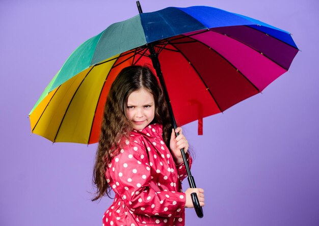 Fröhliches Hipster-Kind in positiver Stimmung Regenschutz Regenbogen-Herbstmode glückliches kleines Mädchen mit buntem Regenschirm kleines Mädchen im Regenmantel Die Kraft der Natur spüren