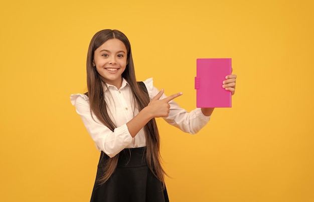 Fröhliches jugendlich Mädchen in Schuluniform, das mit dem Finger auf Buchwerbung zeigt