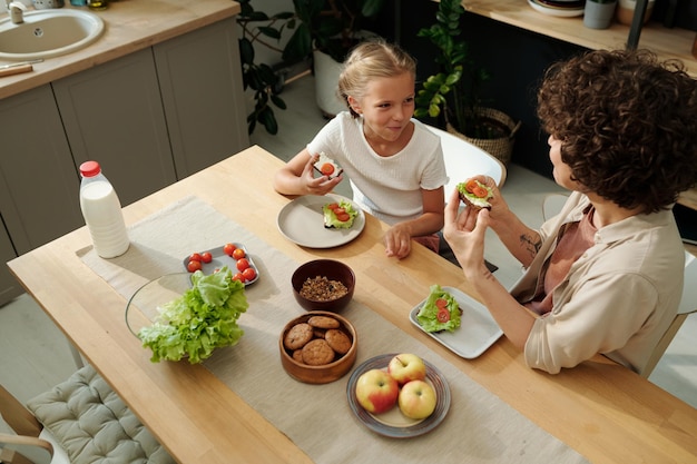 Fröhliches jugendliches Mädchen und ihre Mutter essen Sandwiches mit frischem Gemüse