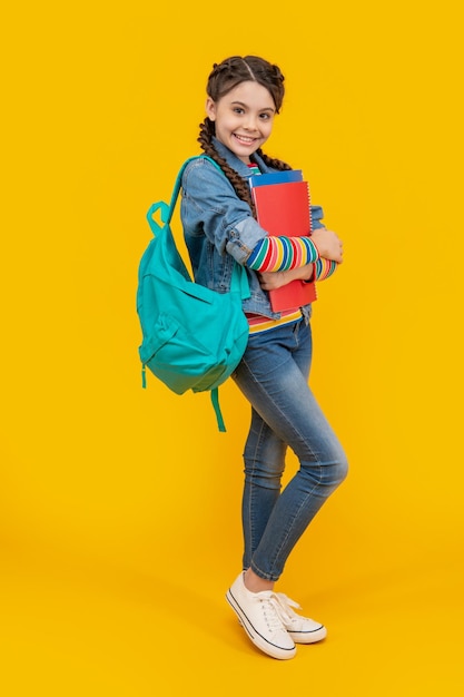 Fröhliches jugendliches Schulmädchen mit gelbem Hintergrund. Heranwachsendes Mädchen zurück in der Schule. Heranwachsender Schüler hält Bücher in der Hand. 1. September Tag des Wissens