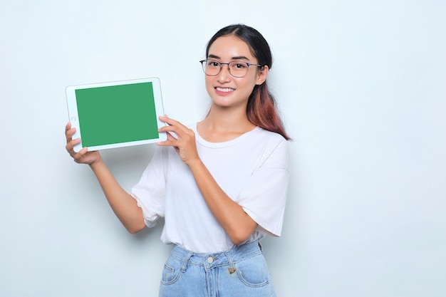 Fröhliches junges asiatisches Mädchen im weißen T-Shirt mit digitalem Tablet mit leerem Bildschirm isoliert auf weißem Hintergrund