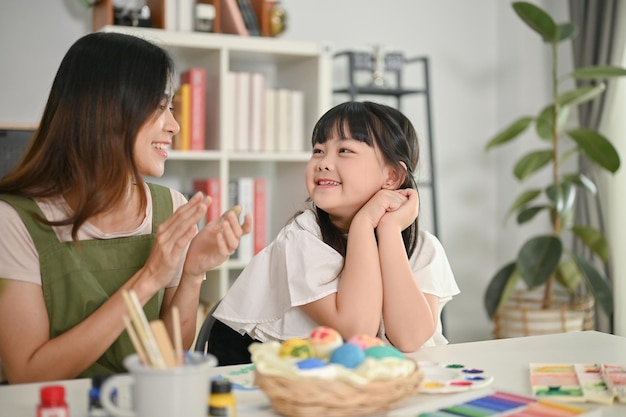 Fröhliches junges asiatisches Mädchen und ihre Mutter, die Ostereier für den Urlaub vorbereiten