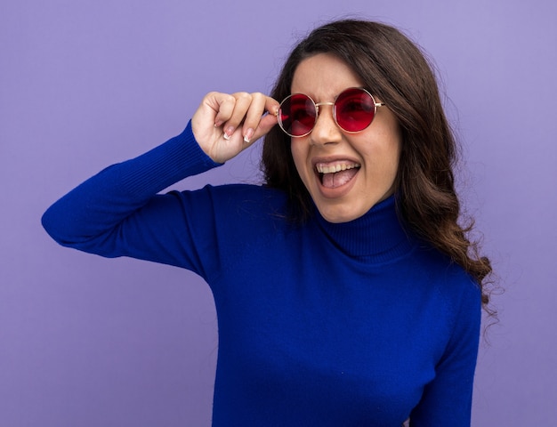 Fröhliches junges hübsches Mädchen mit Sonnenbrille, das eine Brille mit Blick auf die Seite greift