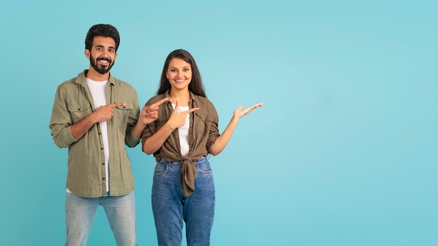 Fröhliches junges indisches Paar, das auf den bunten Hintergrund des Kopierraums zeigt