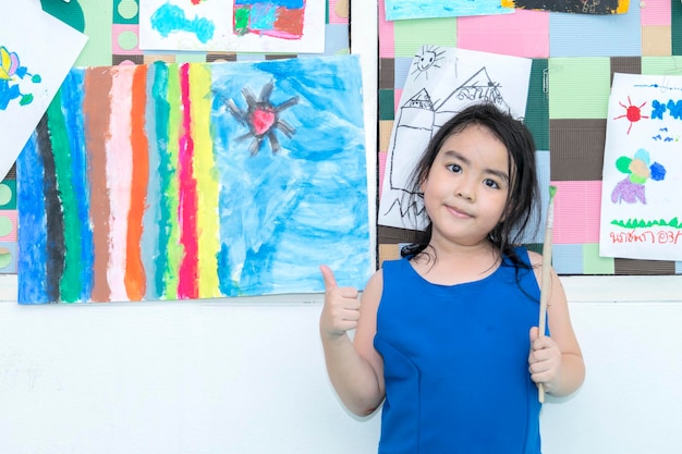 Fröhliches junges Mädchen, das an der Wand maltKunstunterricht im KindergartenPorträt eines entzückenden kleinen Mädchens, das glücklich lächelt, während es den Kunst- und Handwerksunterricht in der Vorschule genießt und zusammenarbeitet