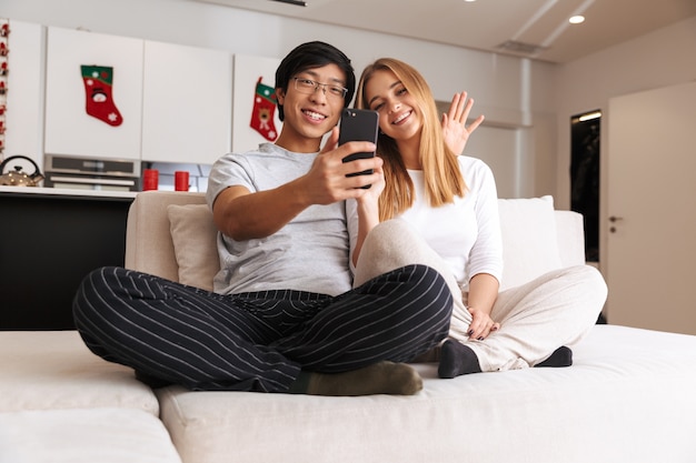 Fröhliches junges Paar, das ein Selfie macht, während es zu Hause auf einer Couch sitzt