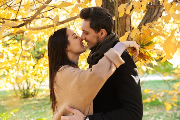 Fröhliches junges Paar, das im Herbst lustige Zeit im Park verbringt, sich umarmt, küsst