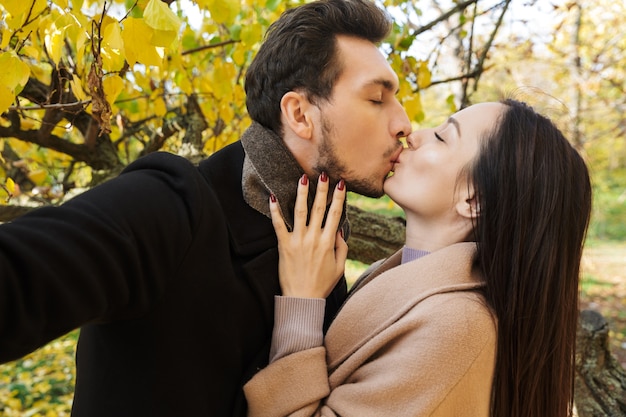 Fröhliches junges Paar, das im Herbst Spaß im Park verbringt und ein Selfie macht