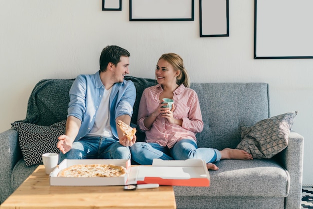 Fröhliches junges Paar, das Pizza auf der Couch isst