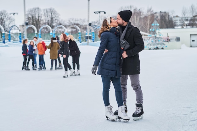 Fröhliches junges Paar, das sich in der Eisbahn verabredet, sich umarmt und die Winterzeit genießt