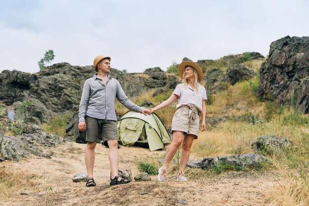 Fröhliches junges Paar Reisende in lässigen Outfits mit Zelt auf dem Berghintergrund Lokal