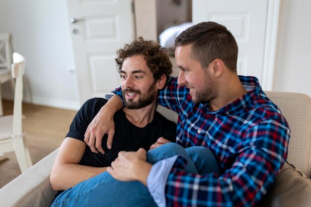 Fröhliches junges schwules Paar, das zusammen sitzt Zwei liebevolle männliche Liebhaber, die fröhlich lächeln, während sie sich umarmen Junges homosexuelles Coupé, das romantisch ist