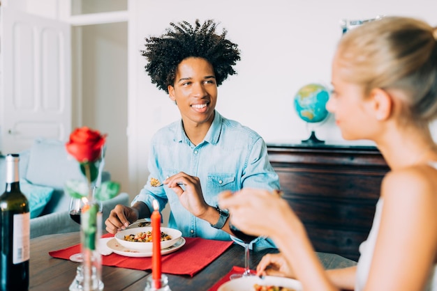 Fröhliches junges verliebtes gemischtrassiges Paar, das an einem romantischen Abendessen teilnimmt