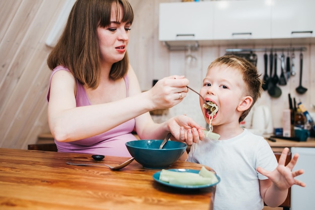 Fröhliches Kind, das mit Mama Nudeln in der Küche isst