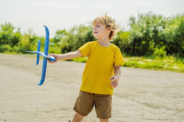 Fröhliches Kind, das mit Spielzeugflugzeug vor altem Start- und Landebahnhintergrund spielt Reisen mit Kinderkonzept