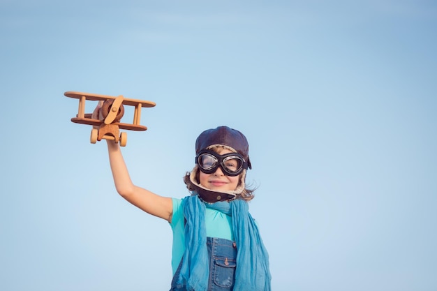 Fröhliches Kind, das mit Spielzeugflugzeug vor sommerlichem Himmelshintergrund spielt Reisekonzept