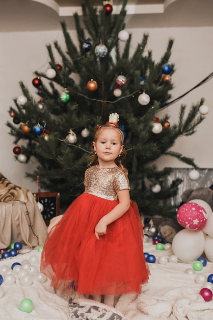 Fröhliches Kind feiert Neujahr und Weihnachten am geschmückten Weihnachtsbaum und Girlanden