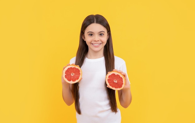 Fröhliches Kind hält Grapefruit auf gelber Hintergrunddiät