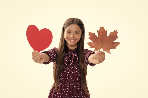 Fröhliches Kind hält Herbstahornblatt und Valentinsherzschatz