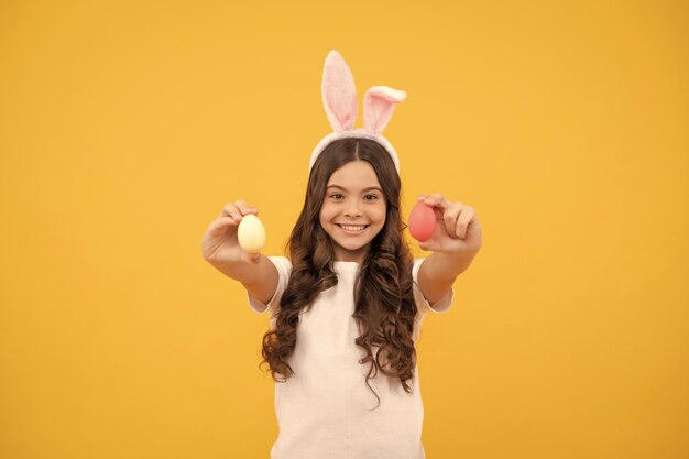 Fröhliches Kind in Hasenohren hält Eier auf gelbem Hintergrund Frohe Ostern