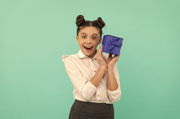 Fröhliches Kind in Schuluniform mit Geschenkbox auf blauem Hintergrund Geburtstag