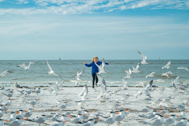 Fröhliches Kind läuft mit Möwenvögeln und vergnügt sich an einem heißen Sommertag im Sommerurlaub am Strand