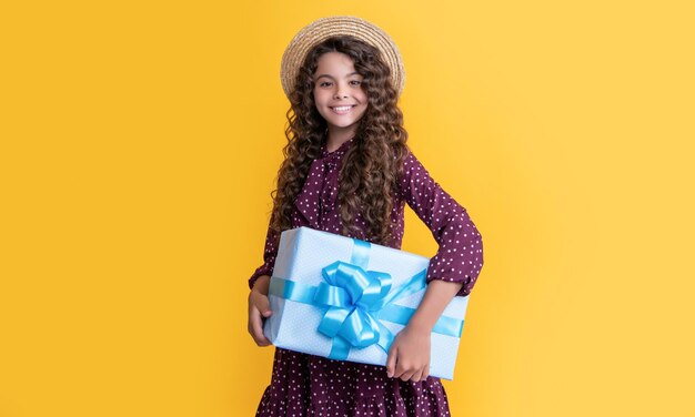 Fröhliches Kind mit lockigem Haar hält Geschenkbox auf gelbem Hintergrund