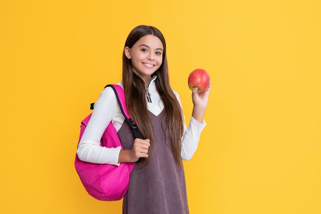 Fröhliches Kind mit Schulrucksack und Apfel auf gelbem Hintergrund