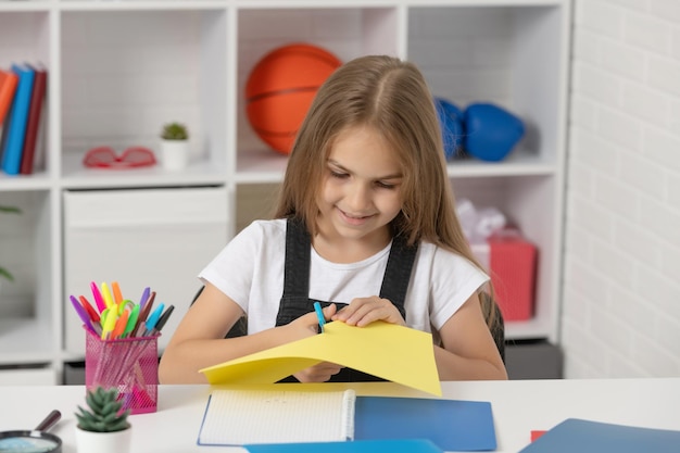 Fröhliches Kind schnitt Papier im Schulklassenzimmer