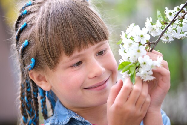 Fröhliches Kindermädchen, das im Frühlingsgarten spielt und an einem sonnigen Tag den süßen Duft der blühenden Blumen des weißen Kirschbaums genießt