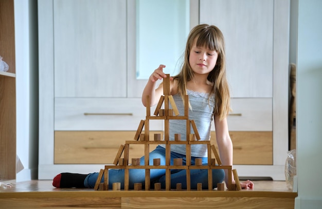 Fröhliches Kindermädchen, das Spiel stapelt, Holzspielzeugblöcke in Hochstapelstruktur stapelt Handbewegungskontrolle und Aufbau eines Konzepts für Rechenfähigkeiten