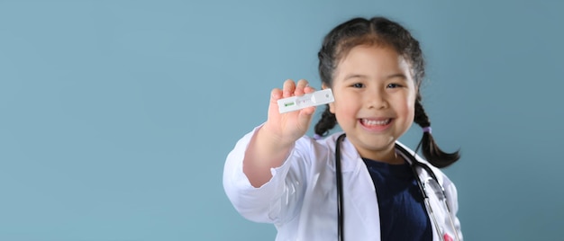 Fröhliches kleines asiatisches Mädchen mit Antigen-Schnelltest-Kit mit negativem Ergebnis während des COVID-19-Tupfertests. Coronavirus Self nasal oder Home Test, Lockdown und Home Isolation Konzept