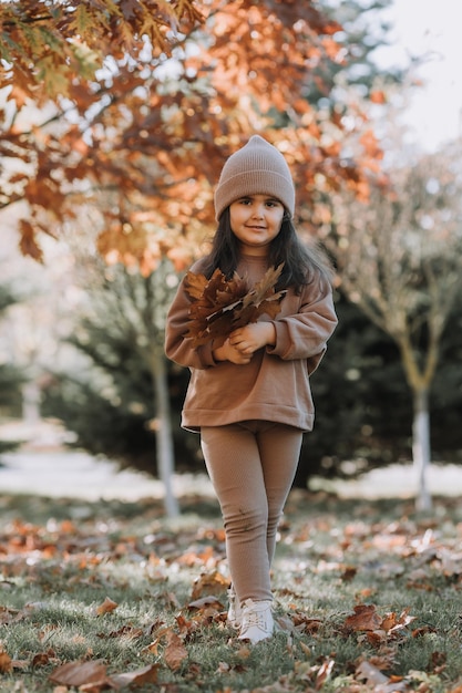 Fröhliches kleines brünettes Mädchen mit Strickmütze geht im Herbst im Park spazieren