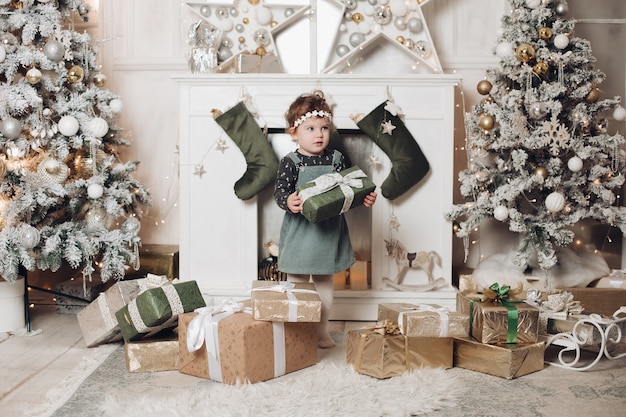Fröhliches kleines Kind hält ein Weihnachtsgeschenk und freut sich über Weihnachtsatmosphäre