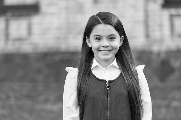 Fröhliches kleines Kind mit langem Haarlächeln in Schuluniform Herbsttag im Freien am 1. September