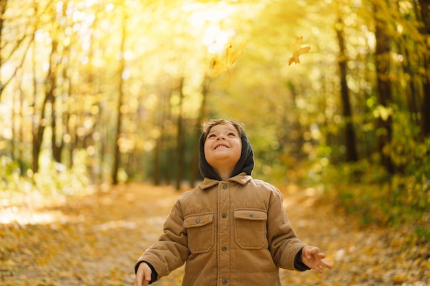 Fröhliches kleines Kinderbaby, das am Herbsttag lacht und spielt Kinderspiel mit Blättern