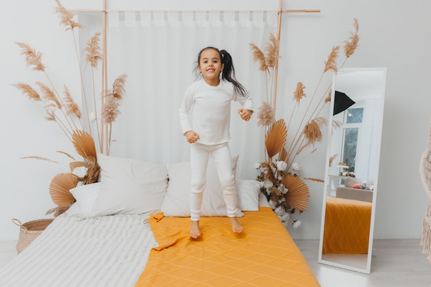 Foto fröhliches kleines mädchen, das auf das bett springt. auf dem weißen bett hat das mädchen spaß und springt. kleines kind springt auf weißes bett