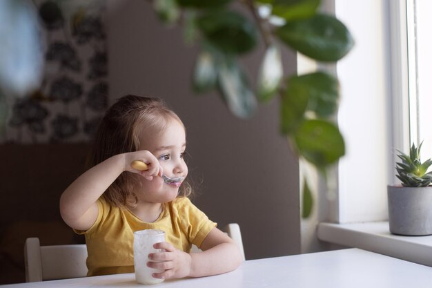 Foto fröhliches kleines mädchen, das einfachen hausgemachten joghurt mit einem löffel isst. gesundes lächelndes kind aus biologischem anbau