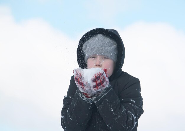 Fröhliches kleines Mädchen, das im Winter auf dem Land mit Schnee im Freien spielt