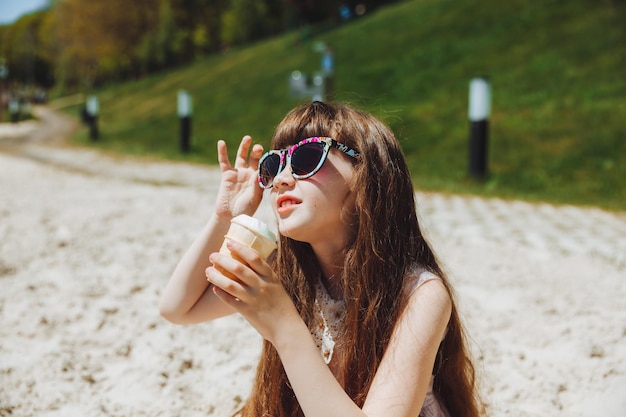 Fröhliches kleines Mädchen, das in den Sommerferien Eis am Strand isst