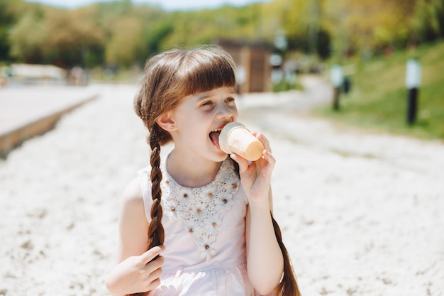 Fröhliches kleines Mädchen, das in den Sommerferien Eis am Strand isst