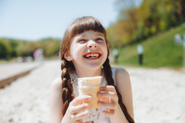 Fröhliches kleines Mädchen, das in den Sommerferien Eis am Strand isst