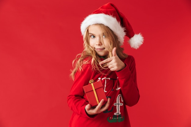 Fröhliches kleines Mädchen, das Weihnachtskostüm trägt, das isoliert steht und Geschenkboxen hält