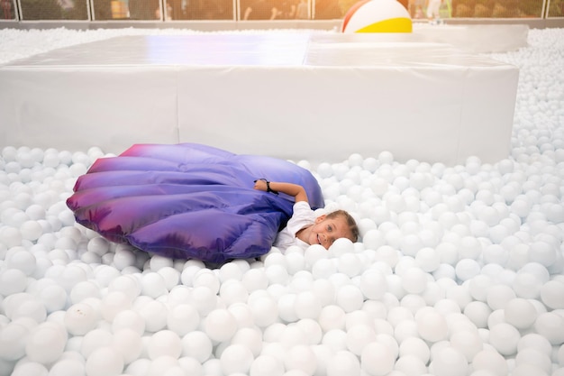 Fröhliches kleines Mädchen, das weiße Plastikbälle auf dem Spielplatz des Vergnügungsparks für Kinder spielt