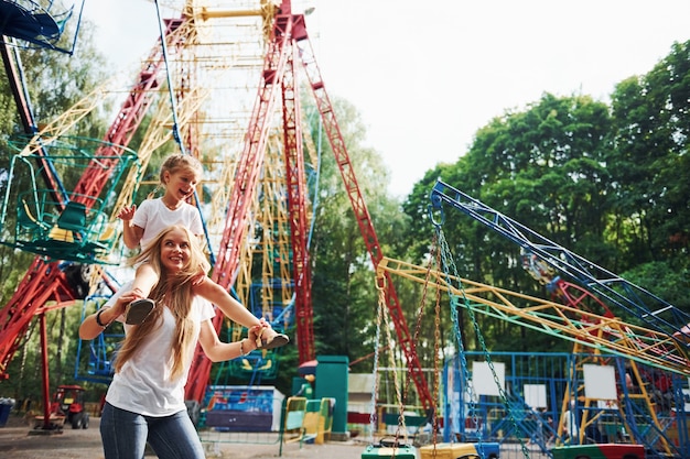 Fröhliches kleines Mädchen, ihre Mutter, haben eine gute Zeit im Park zusammen in der Nähe von Attraktionen.