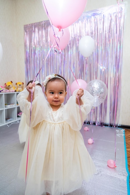 Fröhliches kleines Mädchen im wunderschönen Kleid, das an ihrem Geburtstag mit Luftballons spielt