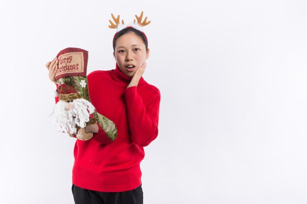 Fröhliches kleines Mädchen in Weihnachtskostüm, das isoliert vor rotem Hintergrund steht und Geschenke von einer Weihnachtssocke nimmt