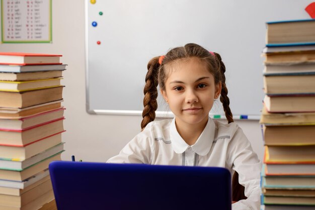 Fröhliches kleines Mädchen in weißer Bluse sitzt am Tisch und macht Schulaufgaben