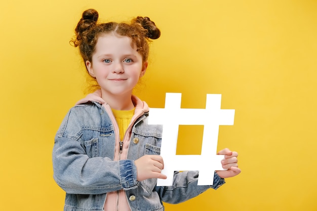 Fröhliches kleines Mädchen mit einem weißen Hashtag auf gelbem Hintergrund